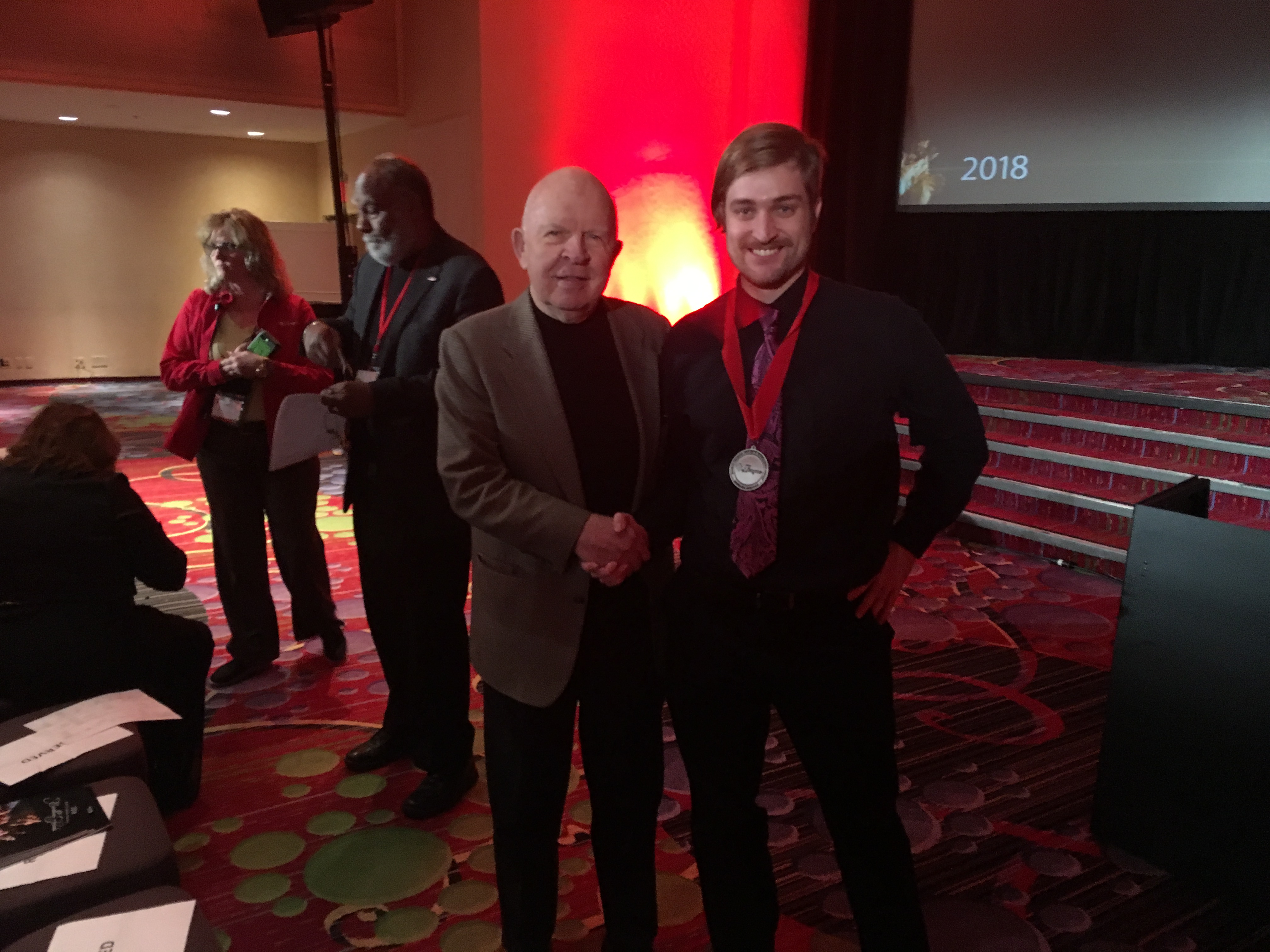 Colburn wearing award medallion shaking hands with John Rouche